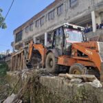 ऊंचापुल में नाले की दीवार से अतिक्रमण ढहाता प्राधिकरण की जेसीबी।